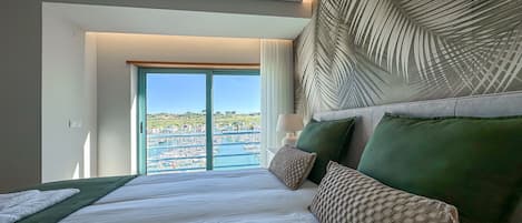 Ett hotellrum med en stor säng, utsikt över en småbåtshamn och en sänggavel med tropiskt tema.