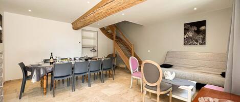 A dining area with a wooden ceiling, a staircase, a sofa, and a wall-mounted artwork.