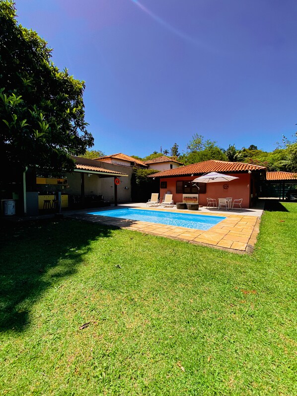 Un patio trasero con piscina, un porche cubierto y un césped.