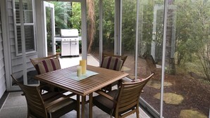 Ein Wintergarten mit Holztisch und -stühlen, einem Grill im Freien und großen Fenstern.