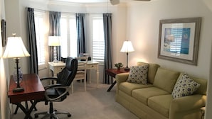 Ein Wohnzimmer mit Schreibtisch, Bürostuhl, Sofa und zwei Lampen.