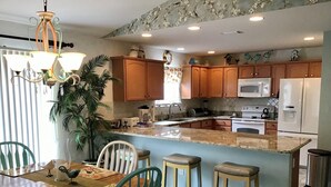 A kitchen with wooden cabinets, a central island, and a dining area with chairs and a table. - 435 Flossmoor Court (The Villages)