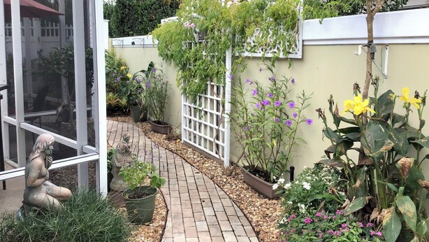 A garden with a paved walkway, potted plants, and a statue. - 435 Flossmoor Court (The Villages)