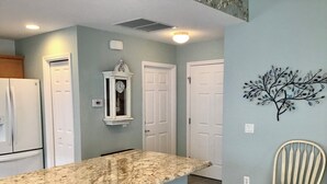 A kitchen with a granite countertop, a clock, and a decorative tree wall art. - 435 Flossmoor Court (The Villages)