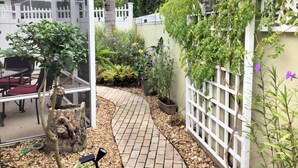A patio area with a table and chairs, a white fence, and various plants and flowers. - 435 Flossmoor Court (The Villages)