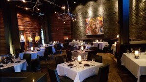 Restaurante com mesas preparadas para refeições, uma pintura grande na parede e decoração em madeira.