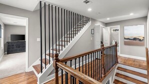 Escadaria moderna com corrimãos de madeira e vista para uma sala de estar com televisão e um armário escuro.