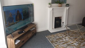 Ett vardagsrum med en TV på ett träställ, en öppen spis och en mönstrad matta.