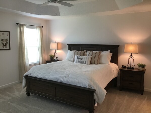 A neatly made bed with a dark headboard, two bedside tables with lamps, a ceiling fan, and a window with curtains. - 2173 Biller Cir (Wildwood)