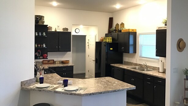 Une cuisine moderne avec des meubles de couleur sombre, un plan de travail en granit et un îlot central doté de tabourets de bar.