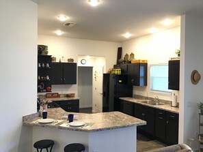 A modern kitchen with dark cabinets, a granite countertop, and a central island with bar stools. - 2173 Biller Cir (Wildwood)