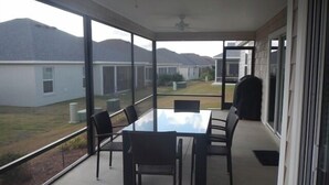 A covered patio with a glass table and chairs, offering a view of neighboring houses and hills. - 1416 Hillstream St (Wildwood)