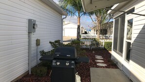 A barbecue grill in a backyard with white siding houses, a white picket fence, and a palm tree. - 2816 Burgos Dr (The Villages)