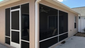 Eine überdachte Terrasse mit Schiebeg lass-Türen, einem Deckenventilator und einem weißen Zaun im Hintergrund.