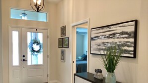 A hallway with a white door, a black console table with a vase and a welcome sign, and a framed abstract painting on the wall. - 2498 Lynette Avenue (Wildwood)