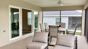 A sunlit patio with a sliding glass door, a ceiling fan, and a table with chairs. - 2498 Lynette Avenue (Wildwood)