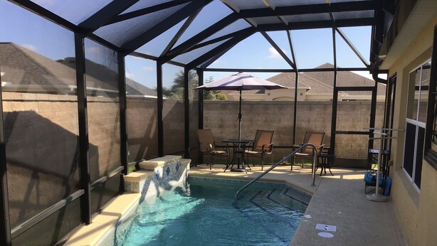 Una piscina exterior techada con un trampolín, sillas de descanso y una mesa de patio.