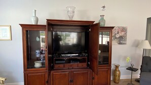 A living room with a wooden entertainment center, a television, and decorative items. - 2351 Bayberry Ct (The Villages)