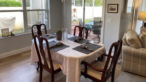 A dining area with a table set for four, surrounded by wooden chairs, a chandelier, and a view through a glass door to an outdoor patio. - 2351 Bayberry Ct (The Villages)