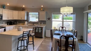 A modern kitchen with white cabinets, a central island with bar stools, a chandelier, and a dining area with a table and chairs. - 2351 Bayberry Ct (The Villages)
