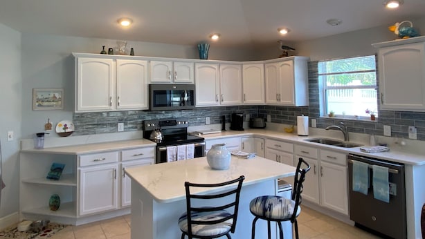 A modern kitchen with white cabinets, a central island, a microwave, and a dishwasher. - 2351 Bayberry Ct (The Villages)