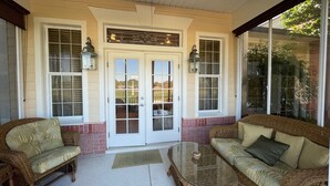 A covered porch with wicker furniture, a glass-top table, and a double door with glass panels. - 1504 Wresh Way (The Villages)