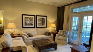 A living room with a sofa, two armchairs, a coffee table, and a side table with lamps. There are two framed pictures on the wall, and a door leading to a balcony. - 1504 Wresh Way (The Villages)