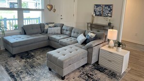 Een moderne woonkamer met een modulaire bank, een passende poef, een bijzettafeltje met een lamp en een decoratief wandobject.
