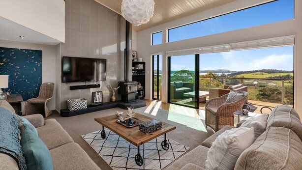 A spacious living room with a large sofa, a coffee table, and a fireplace. There is a television mounted on the wall and a large window offering a view of the outdoors.