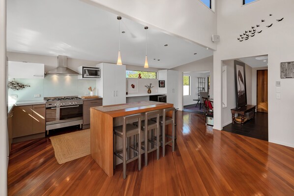A modern kitchen with a central island, stainless steel appliances, pendant lighting, and a wooden floor.