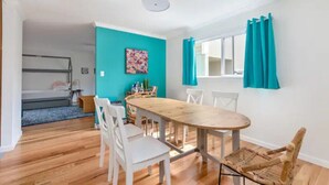 A room with a wooden dining table, white chairs, a teal accent wall, a window with teal curtains, and a bunk bed in the background. - Game room, hot tub, 20 min to SF, beach 1 block away (Pacifica)