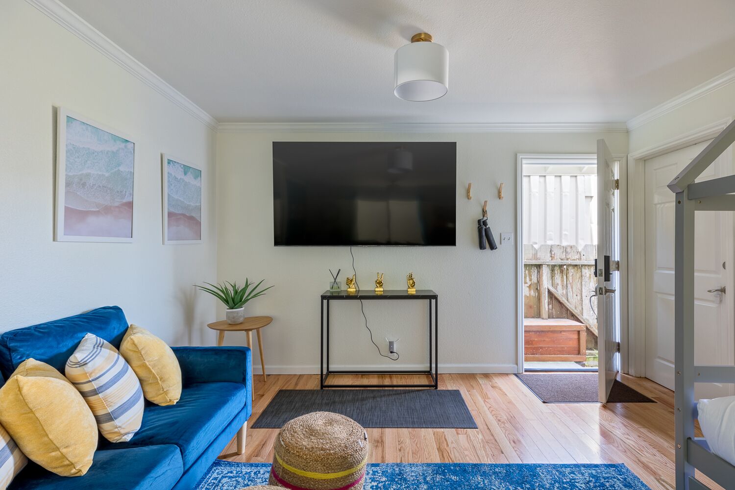 A living room with a blue sofa, a small side table with a plant, a mounted TV, and a staircase leading to an outdoor area.