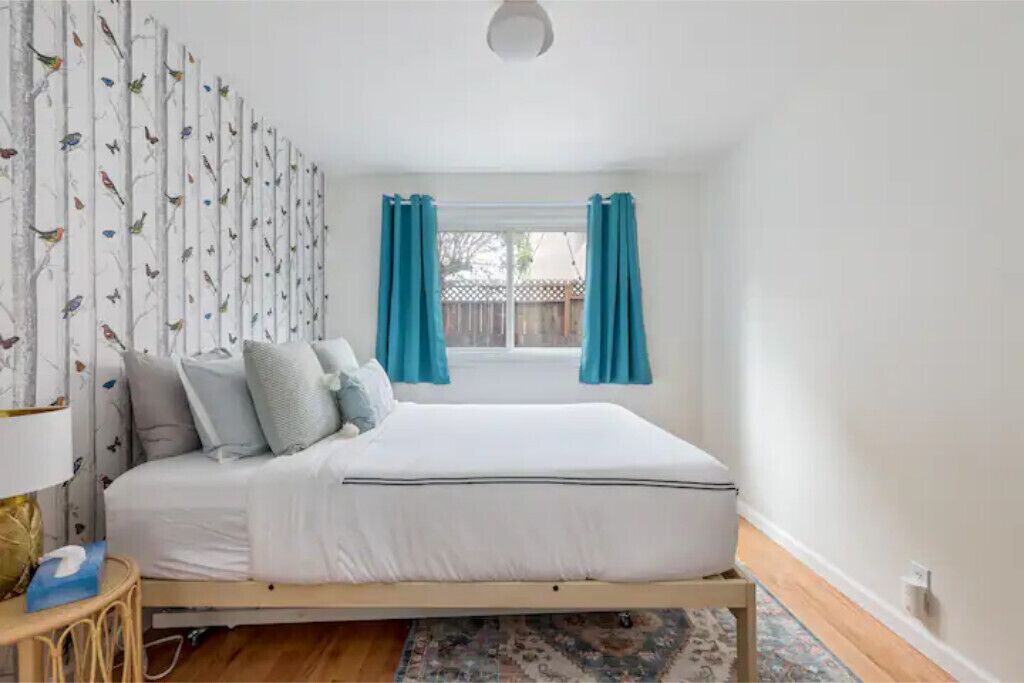 Une chambre à coucher avec un lit, une fenêtre avec des rideaux et un mur orné d’un motif représentant des oiseaux.