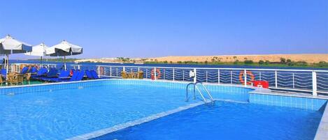 A swimming pool with blue tiles, a metal ladder, and lounge chairs.