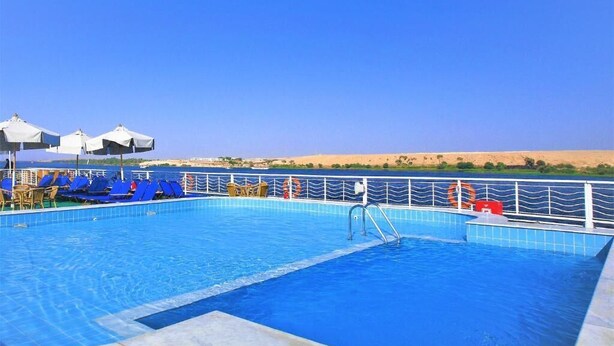 Uma piscina com azulejos azuis, uma escada e espreguiçadeiras.