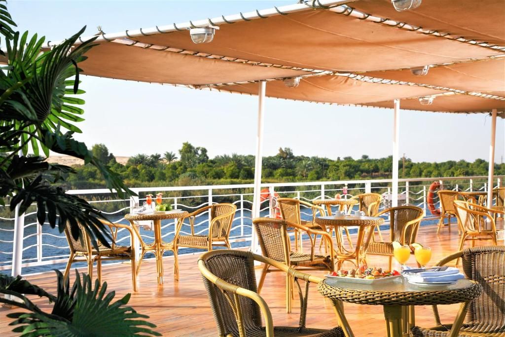 An outdoor dining area with wicker furniture and umbrellas, overlooking a body of water.
