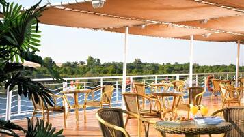 An outdoor dining area with wicker furniture and umbrellas, overlooking a body of water.