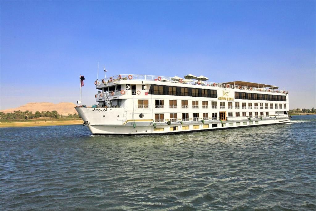 Um grande navio de cruzeiro fluvial com vários decks, botes salva-vidas e uma bandeira.