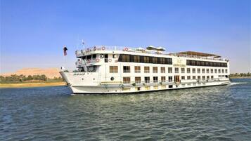 Um grande navio de cruzeiro fluvial com vários decks, botes salva-vidas e uma bandeira.