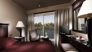 Quarto de hotel com uma cama grande, uma escrivaninha com uma TV, uma cadeira e vista para o exterior.
