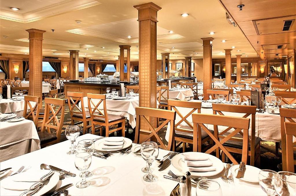 Spaziosa sala da pranzo con diversi tavoli e sedie, colonne in legno e un'area bar centrale.