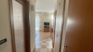 Un pasillo con piso a cuadros, puertas de madera y vista a una sala de estar con televisor y un perro.