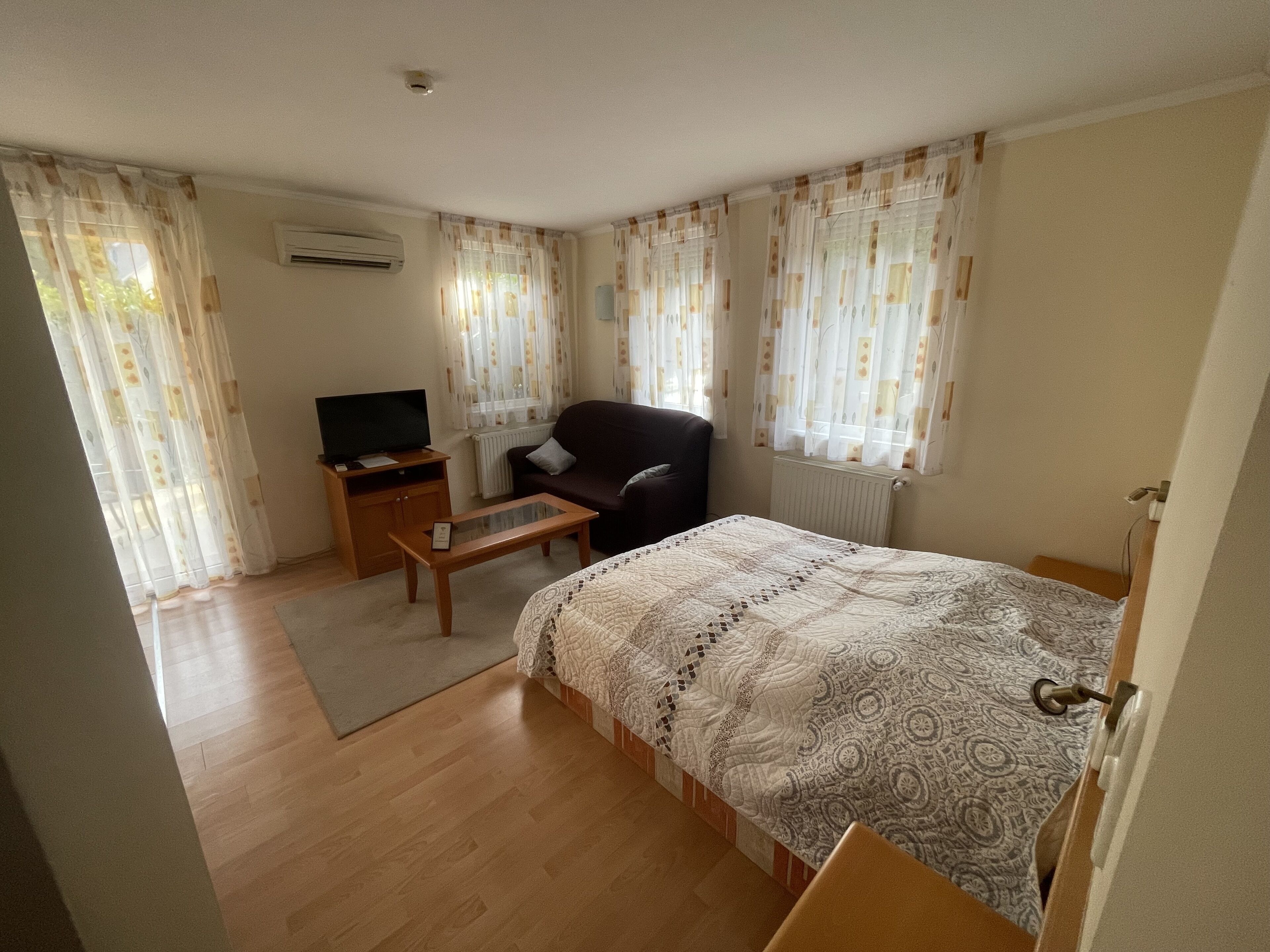 A hotel room with a bed, a TV on a wooden stand, a chair, and a small table.