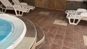 Zona de piscina con sillones de descanso, jacuzzi y una pared de piedra.
