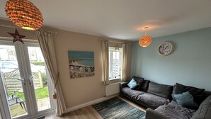 Ein gemütliches Wohnzimmer mit grauem Sofa, einem Gemälde, einer Sterndeko und einer Uhr an der Wand.