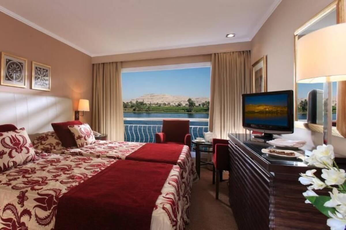 Habitación de hotel con una cama, un escritorio con computadora, televisión y vista hacia el agua.