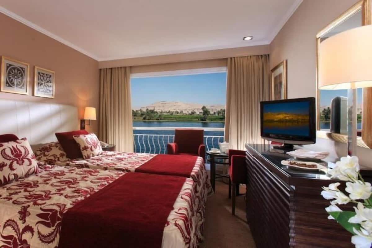 A hotel room with a bed, a desk with a computer, a television, and a view of a body of water.