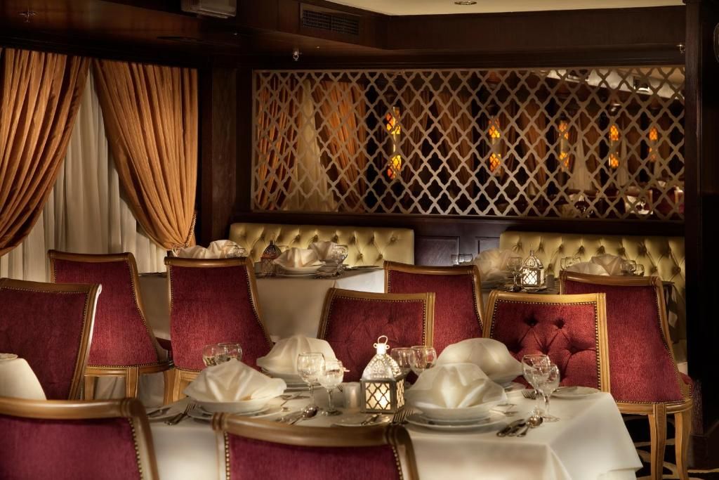 Une salle à manger élégante, avec des chaises à revêtement rouge, des nappes blanches et un paravent décoratif à motifs géométriques.