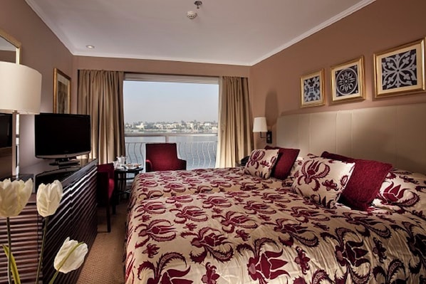 A hotel room with a large bed, a television, a desk, and a view of the city. - Steigenberger Minerva Cruise 4&7 Nights From Luxor (Luxor)
