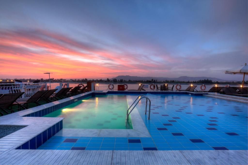 A swimming pool with a view of the sunset, deck chairs, and lifebuoys.